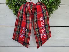 a red plaid christmas bow with the words merry on it hanging from a white wooden wall