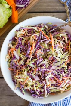 a white bowl filled with coleslaw on top of a wooden table next to a cutting board