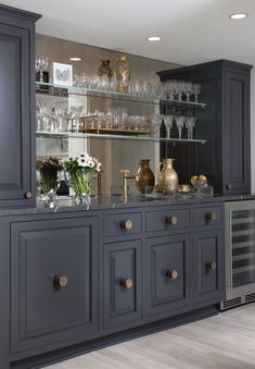 a kitchen with gray cabinets and glass shelves filled with wine glasses, vases and flowers