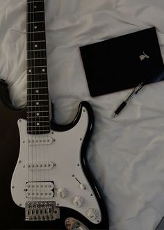 an electric guitar laying on top of a bed next to a notepad and pen