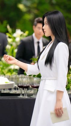 a woman in a white dress standing next to a table with wine glasses on it