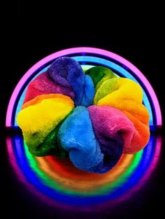 a multicolored teddy bear sitting on top of a rainbow colored object in front of a black background