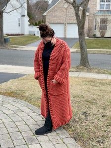 a woman is standing on the sidewalk wearing an orange cardigan