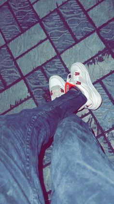 a person wearing white shoes and jeans standing on a tile floor with their legs crossed