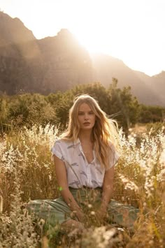 a woman sitting in tall grass with mountains in the background