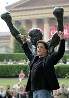 two women standing in front of a statue holding their hands up to the sky with one woman's legs raised