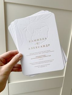 a person holding up some white cards with gold foil on them in front of a door