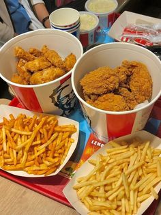 three buckets filled with fried chicken and french fries next to other foods on a table