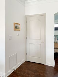 an empty room with a white door and wood floors in front of a mirror on the wall