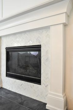 an empty fireplace with a black mantle and white chevron tile