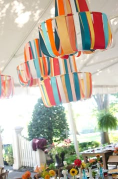 an outdoor dining area with colorful striped lamps hanging from the ceiling and flowers in vases on the table