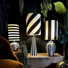 three black and white striped lamps sitting on top of a wooden table next to plants