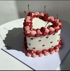 a heart shaped cake with cherries on it sitting on top of a white table