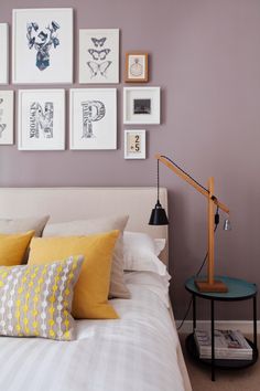 a bed with yellow pillows and pictures on the wall above it, in a bedroom