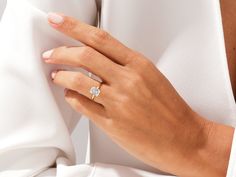 a woman's hand with a diamond ring on her finger, wearing a white dress