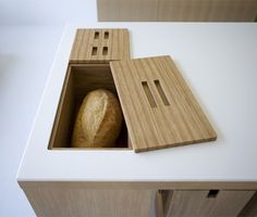 a loaf of bread in a wooden box on top of a white counter next to a knife