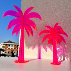 two pink plastic palm trees sitting on top of a white table next to a building