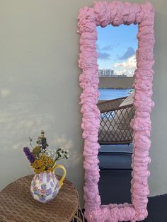 a pink mirror sitting on top of a table next to a vase