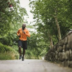 a man running down the road in an orange jacket and black shorts with trees around him