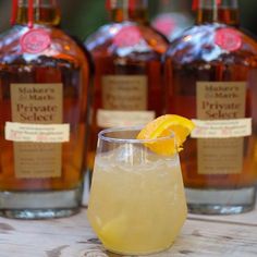 three bottles of maple syrup and a glass with a lemon garnish on the rim