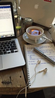 an open laptop computer sitting on top of a wooden desk next to a cup of coffee