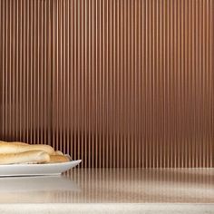 two hotdogs on a white plate in front of a brown wall with vertical stripes