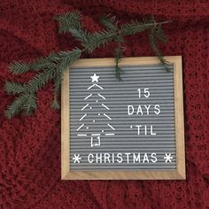 a christmas sign hanging on the side of a red wall next to a fir tree