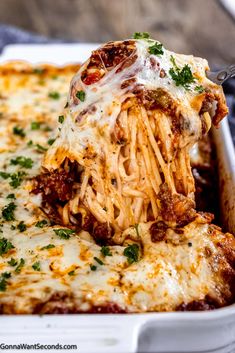 a piece of lasagna being lifted from a casserole dish with meat and cheese