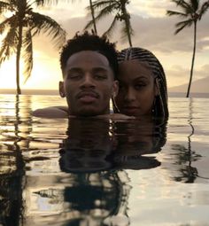 two people are in the water with palm trees behind them and one is looking at the camera