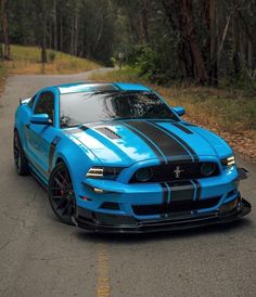 a blue mustang car parked on the side of a road in front of some trees