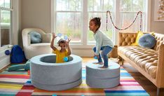 two children playing in a play room with colorful rugs and couches on the floor