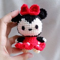 a small crocheted minnie mouse doll in a red dress is held up by someone's hand