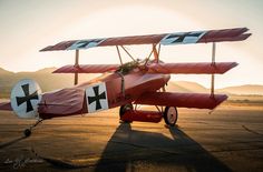 an old red airplane is parked on the tarmac at sunset with mountains in the background