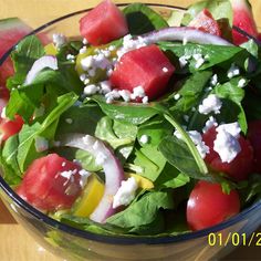 a salad with watermelon, onions and feta cheese in a glass bowl