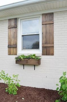 a white brick house with wooden shutters on the windowsill and plants growing in the window boxes