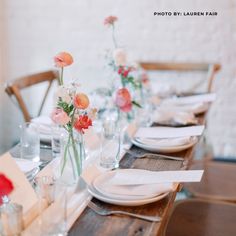 the table is set with white plates and pink flowers in glass vases on them