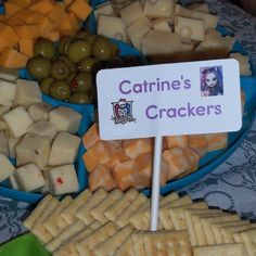 a blue plate topped with crackers covered in cheese and olives next to a sign that says carine's crackers