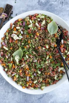 a white bowl filled with lentils and vegetables next to two black serving spoons