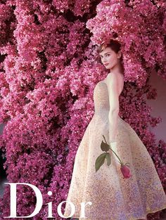 a woman standing in front of pink flowers with the words dior written on it