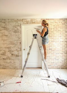 a woman standing on a ladder in front of a brick wall using her cell phone