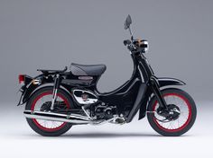 a black motorcycle with red rims parked in front of a gray background