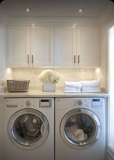 a washer and dryer in a white laundry room with lots of cabinet space