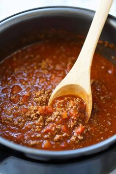 a wooden spoon in a black pot filled with chili and ground beef soup on the stove