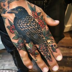 a hand with a black bird on it and red flowers around the wrist is shown