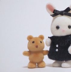 a small teddy bear standing next to a toy rabbit