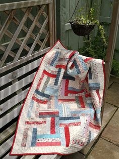 a patchwork quilt on a bench in front of a wooden fence and potted plant