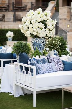 a white couch sitting on top of a lush green field next to a tall vase filled with flowers