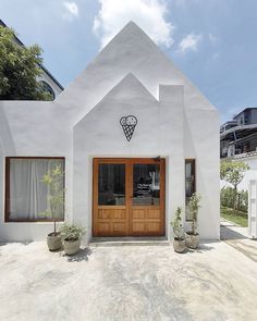 a white building with two wooden doors and plants on the front porch, in front of it