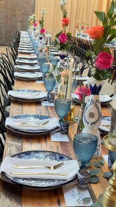 a long table set with blue and white plates, silverware and flowers in vases