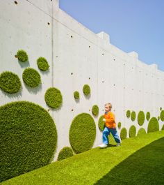 a young boy standing next to a wall covered in grass